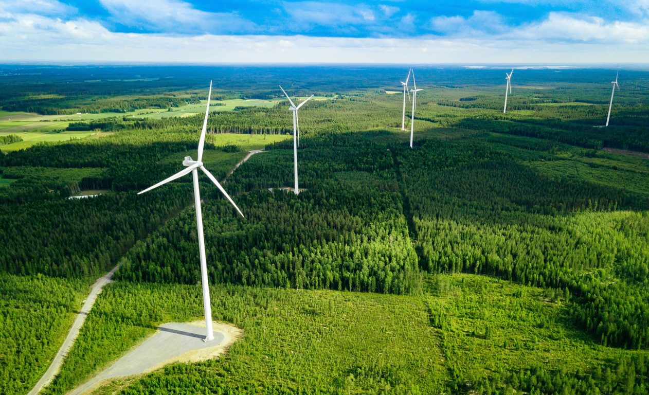 Ilmasta kuvattu valokuva tuulivoimaloista suomalaisen metsän keskellä