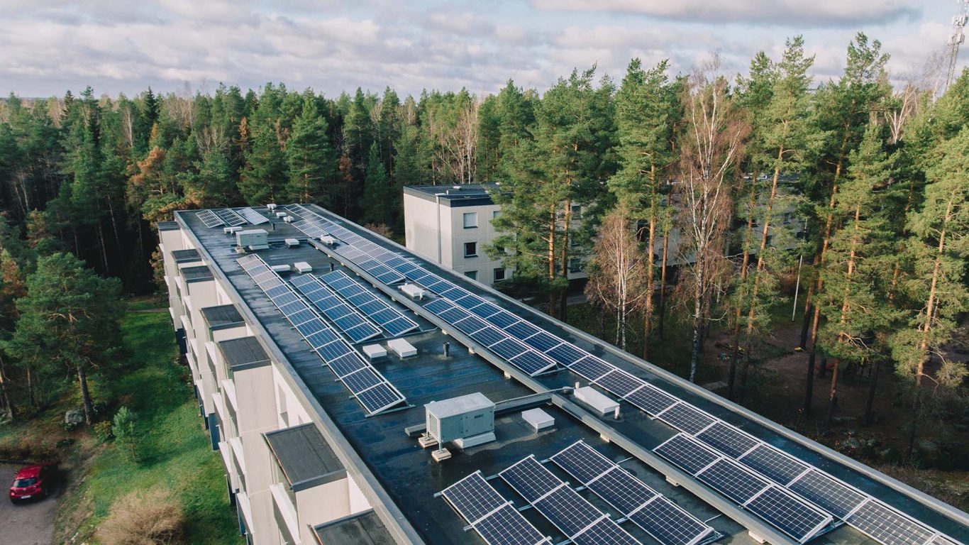 Aurinkopaneelit taloyhtiön katolla. Ilmakuva kerrostalon katosta, jossa aurinkopaneeleja.